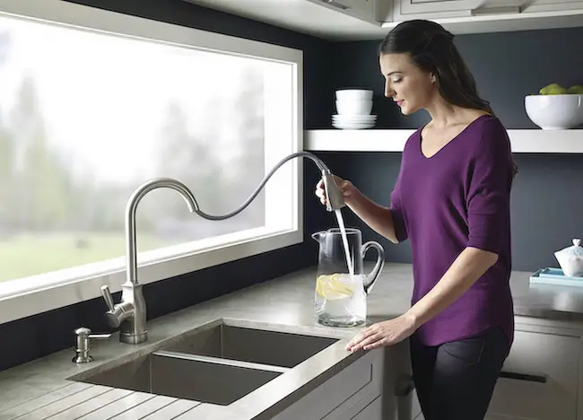 Woman filling a pitcher with clean water after a kitchen plumbing service.
