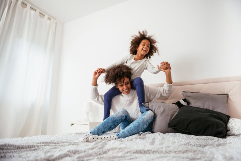 A mother and daughter playing cheerfully together on a bed.