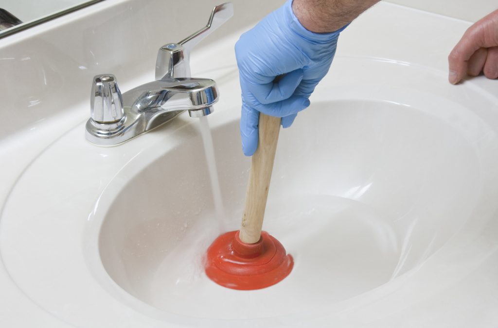 Plumber using a plunger to unplug a bathroom sink with odors